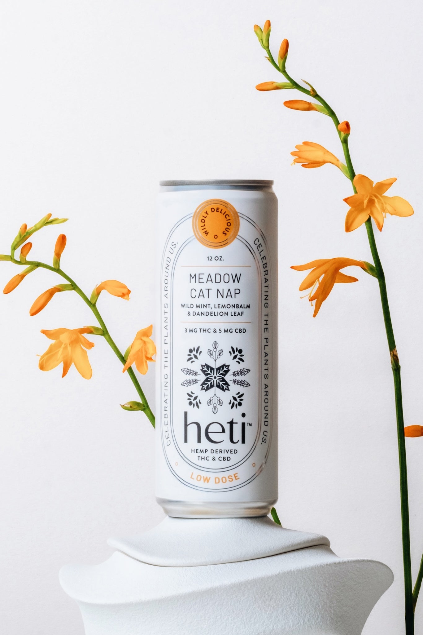 Meadow Cat Nap Heti THC Seltzer Displayed With Yellow and Orange Plants. Made With lemonbalm, wild mint, and dandelion leaf