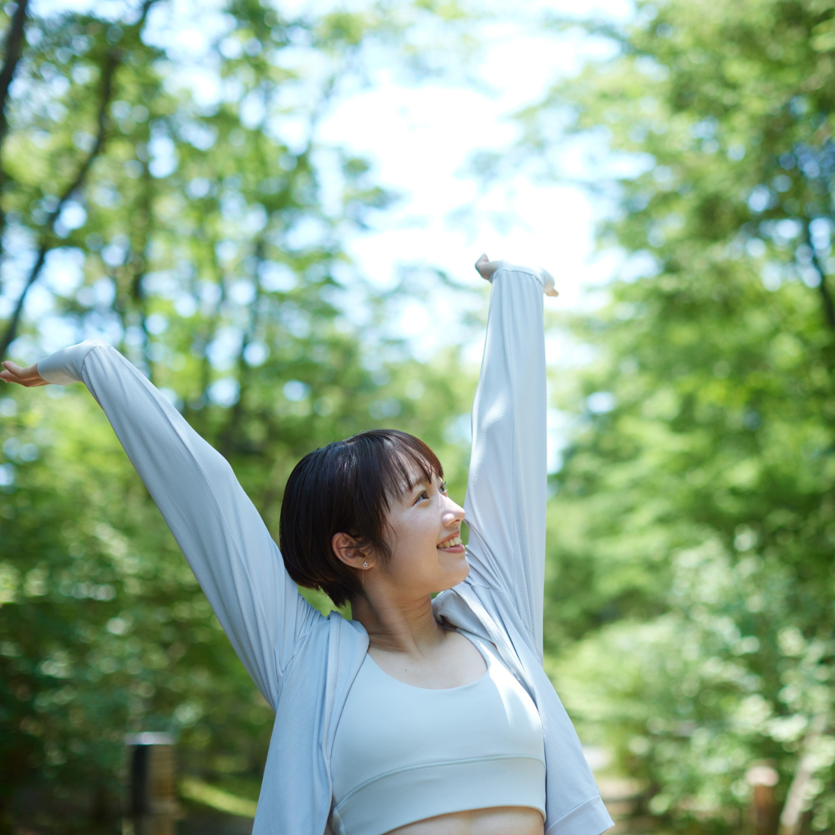Person stretching with arms raised outdoors in a green forest setting, enjoying fresh air and natural light.