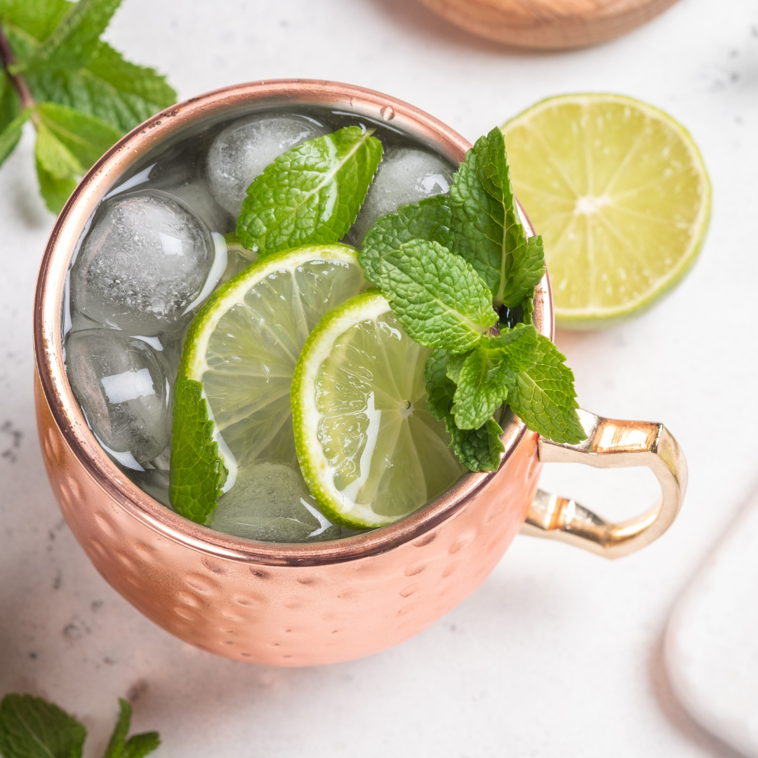 Copper mug filled with ice, topped with lime slices and fresh mint, with a halved lime on the side.