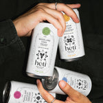 Hands holding four Heti botanical THC beverages River Path, Marshland Harvest, Meadow Cat Nap, and Woodland Edge
