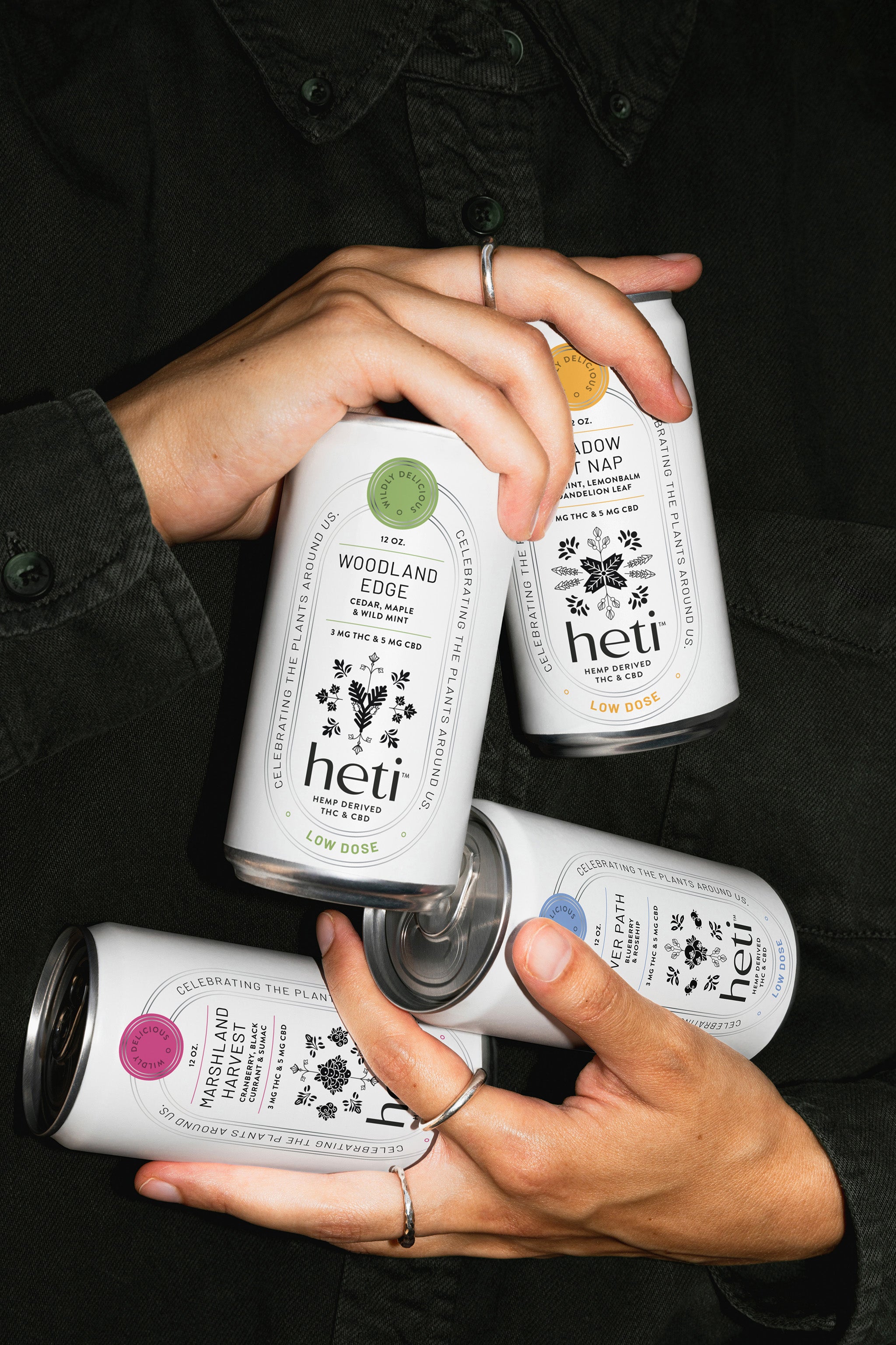 Hands holding four Heti botanical THC beverages River Path, Marshland Harvest, Meadow Cat Nap, and Woodland Edge