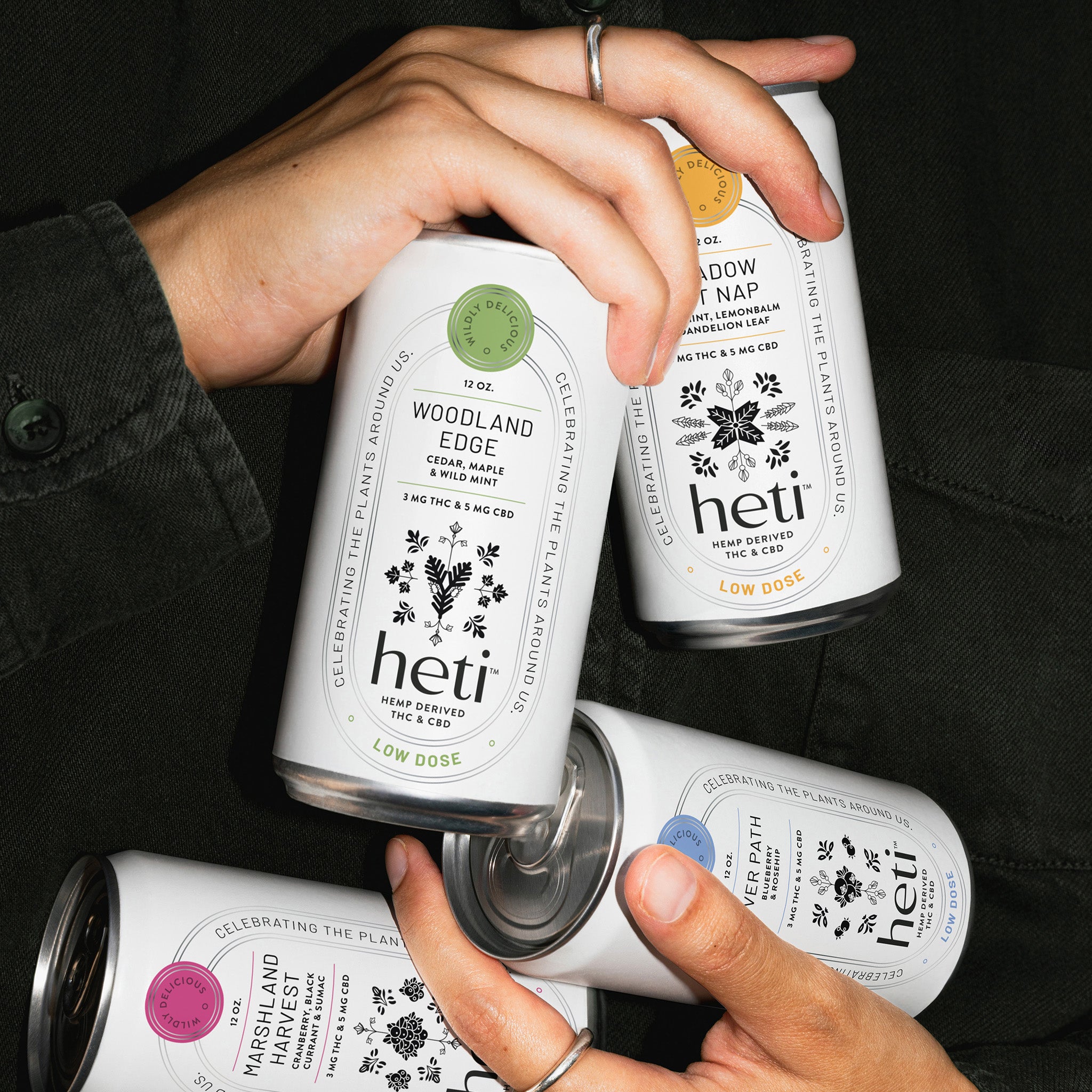 Hands holding all four flavors of Heti THC beverages River Path, Marshland Harvest, Meadow Cat Nap, and Woodland Edge